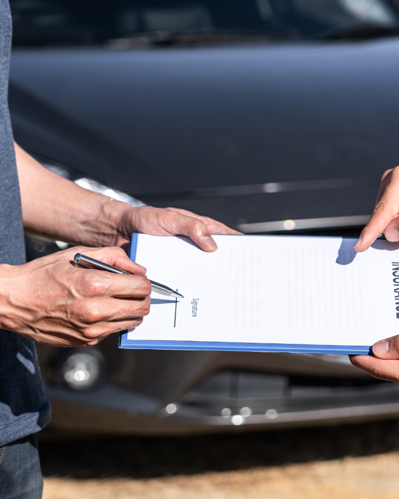 Personas firmando un documento delante de un auto.