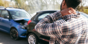 Persona contemplando dos automóviles chocados mientras toca su cuello